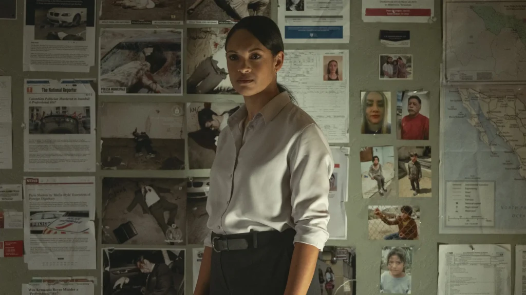 Movie still from The Accountant 2 - Marybeth Medina (Cynthia Addai-Robinson) stands in front of a wall covered with various crime scene photos, notes, and a map, looking contemplative.