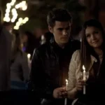 Stefan Salvatore and Elena Gilbert holding candles at the outdoor comet viewing event in Mystic Falls.