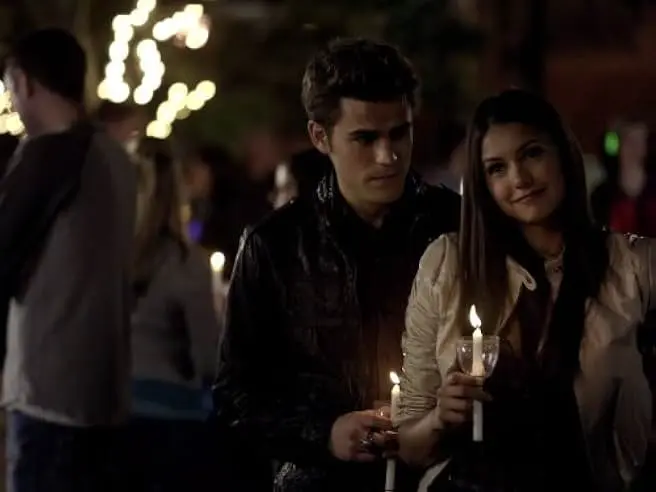 Stefan Salvatore and Elena Gilbert holding candles at the outdoor comet viewing event in Mystic Falls.